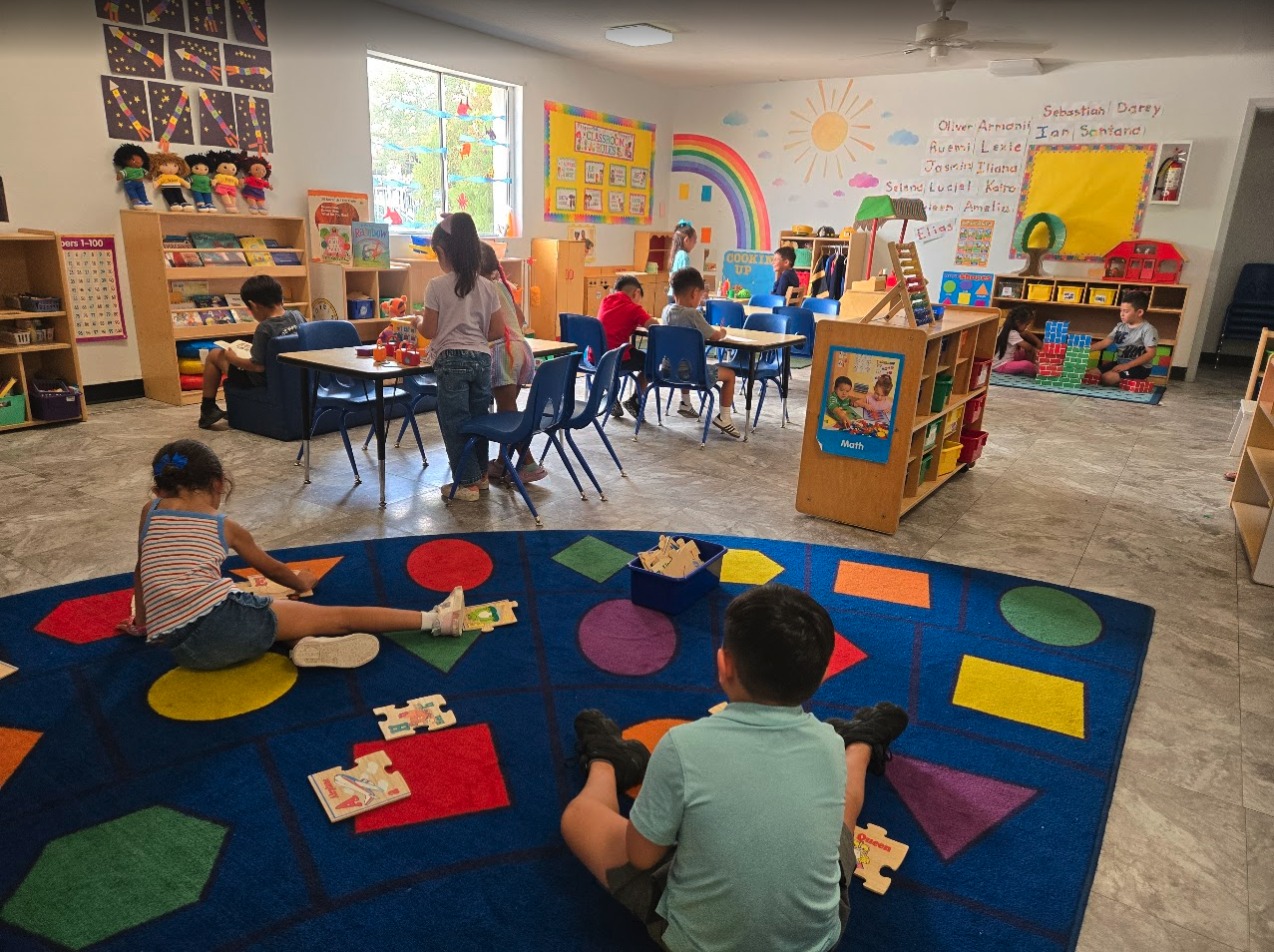 Children playing on a colorful shapes rug in a bright classroom